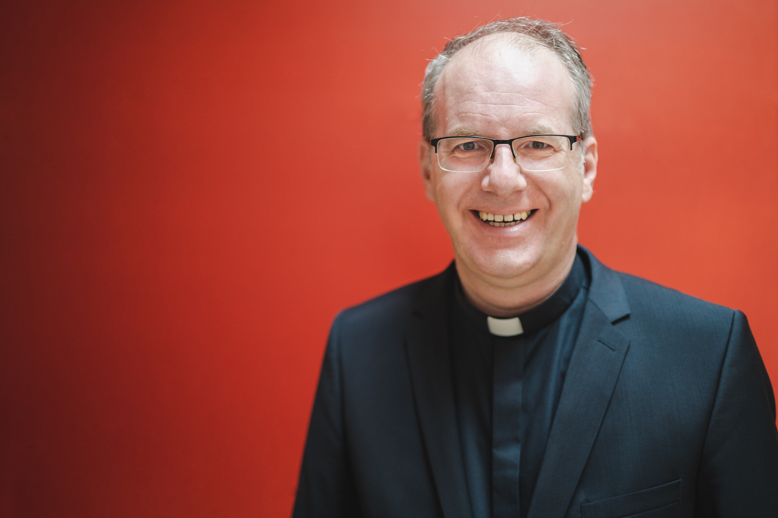 Weihbischof Christian Würtz lachend vor einer roten Wand